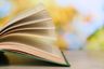 Opened book on wooden table on natural background